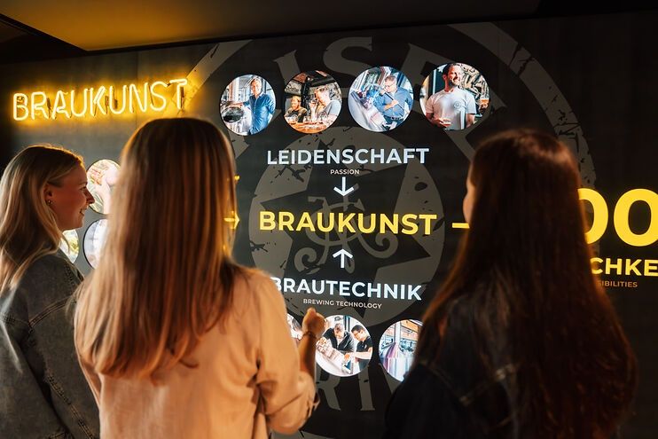 Besucher von Maisel & Friends betrachten einen Bildschirm mit Erklärungen zur Braukunstwelt