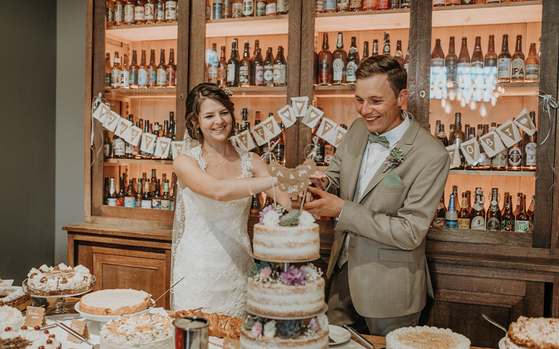 Brautpaar schneidet gemeinsam die Hochzeitstorte vor dekorierter Bar
