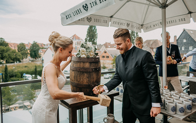 Braut und Bräutigam zapfen Bier aus einem Fass bei der Hochzeit